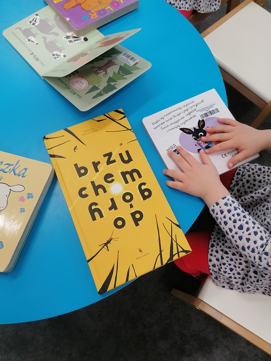 Dłonie dziecka dotykają jednej z czterech książek ułożonych na niebieskim stole