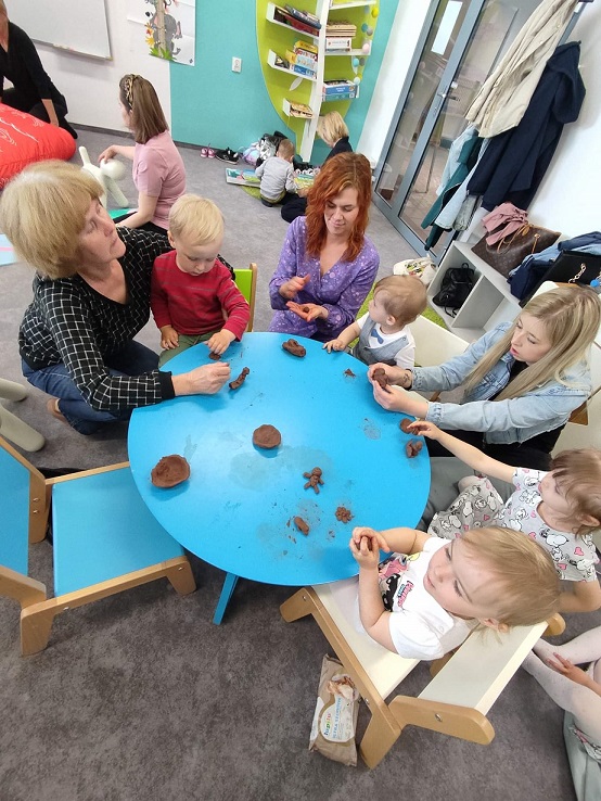 Grupa dzieci z dorosłymi bawią się gliną przy niebieskim stoliku