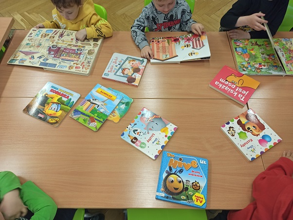 Dzieci siedzą przy stole i przeglądają kolorowe książeczki