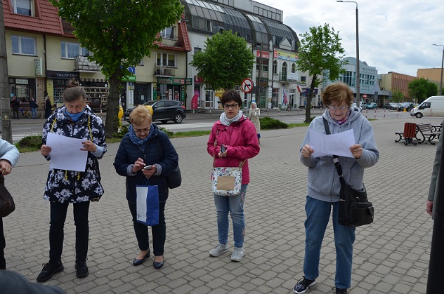 Kilka kobiet stoi na placu przy ratuszu. Dwie z nich przeglądają dawny plan miasta.