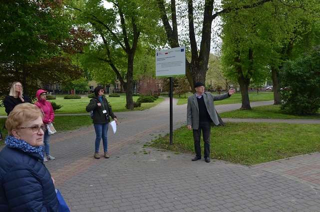 Grupa osób w parku miejskim. Mężczyzna wskazuje ręką obiekt znajdujący się poza kadrem.