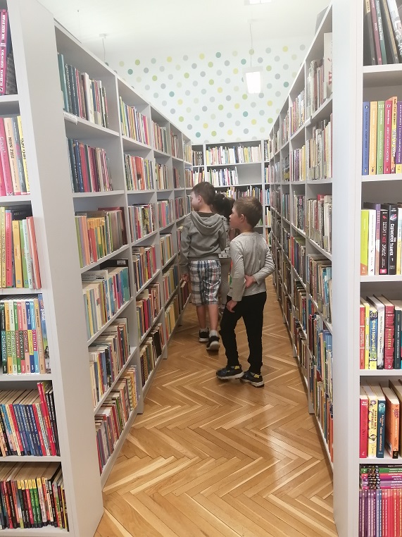 Czwórka dzieci przechadza się między bibliotecznymi półkami z książkami