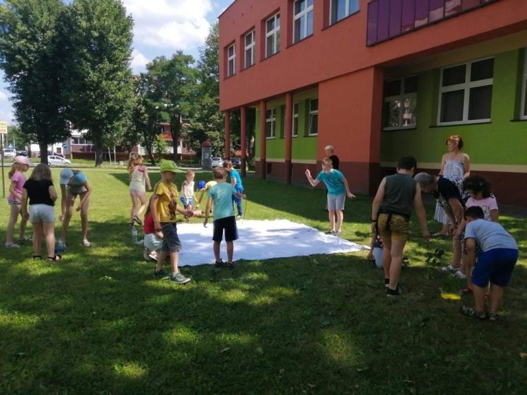 14 uczestników zajęć wakacyjnych "chlapie" obraz na kwadratowym płótnie przed budynkiem biblioteki