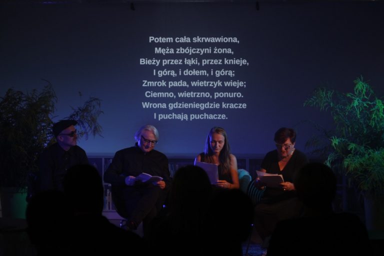 Cztery osoby na pośrodku sceny. Dwóch mężczyzn i dwie kobiety z kartkami w dłoniach. W tle fragment czytanej ballady wyświetlony na ścianie.