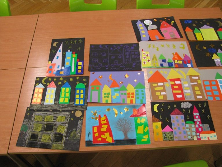 Kolorowe, prace plastyczne pt. "Miasto Nocą" ułożone na części stołu przy którym stoją dwa krzesła