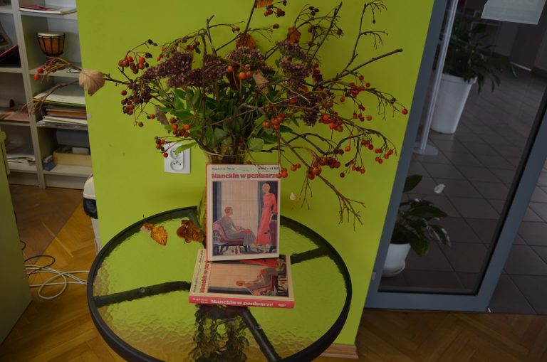 Okrągły stolik, na nim książki i kompozycja z suchych kwiatów i ziół