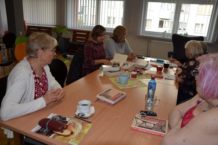 Kilka kobiet siedzi za stołem i dyskutuje przeglądając książki