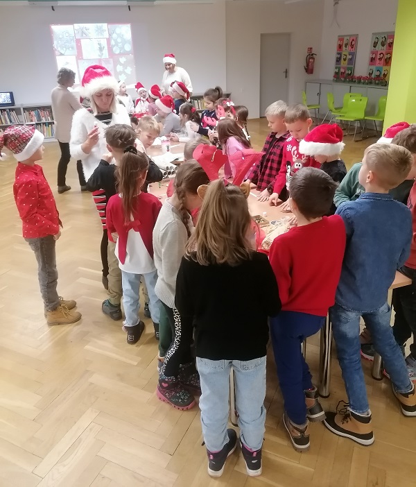Grupy szkolne w strojach mikołajkowych wokół stołu tworzą ozdoby świąteczne