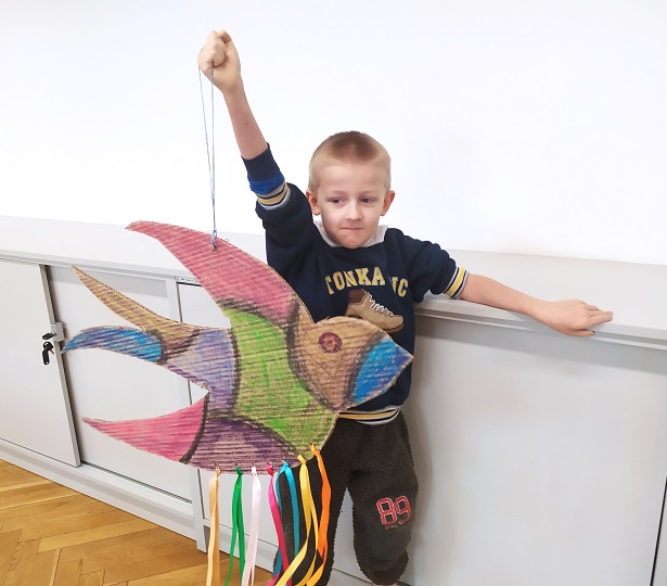 Chłopiec na tle jasnej ściany z kolorową jaskółką wykonaną podczas warsztatów
