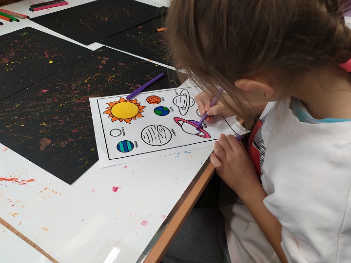Dziewczynka koloruje malowankę z wizerunkami planet