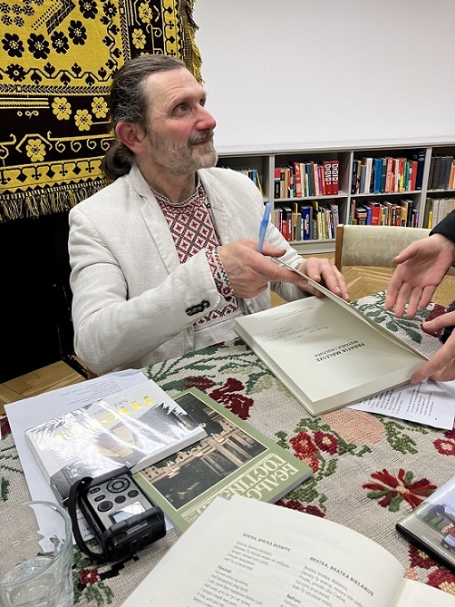 Mężczyzna w białoruskim stroju ludowym podpisuje książki.