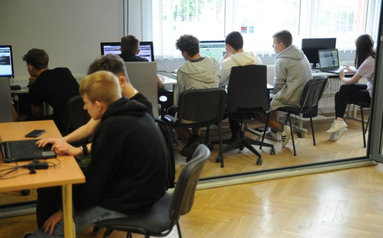 Siedmiu młodych mężczyzn oraz kobieta przy stanowiskach komputerowych