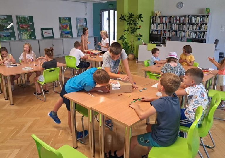 Grupa dzieci przy czterech stolikach w sali bibliotecznej