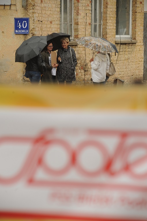 Na pierwszym planie rozmyty baner z logo „Społem”. W głębi pięć kobiet pod parasolami przed ceglanym budynkiem dawnej piekarni nr 1 przy ulicy Adama Mickiewicza. Na ścianie tabliczka z adresem: Mickiewicza 40.