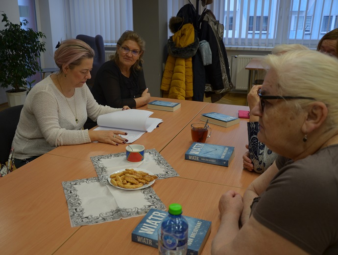 Grupa kobiet siedzi przy stole i rozmawia ze sobą. Na stole książki, kawa, notatki.