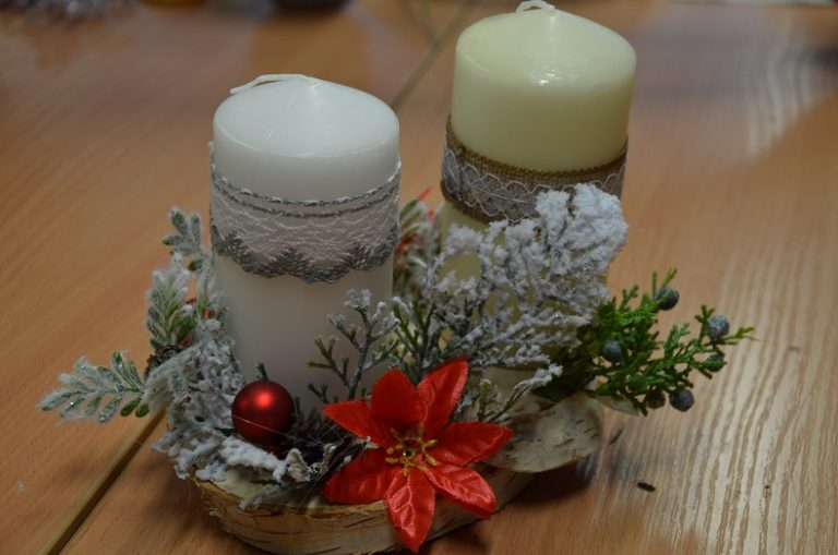Na stole stroik świąteczny z dwiema świecami z ozdobną dekoracją